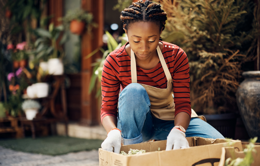 A woman in a red and navy striped shirt looking at a box full of plants with a shop in the background at House of Agave.